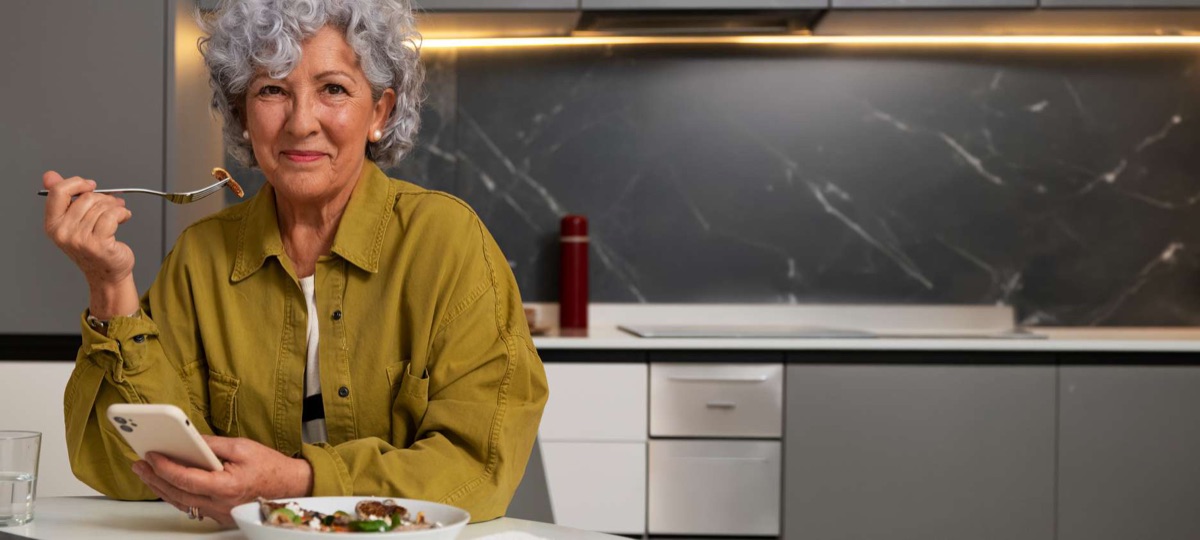 Adulta mayor sonriendo mientras come en su cocina