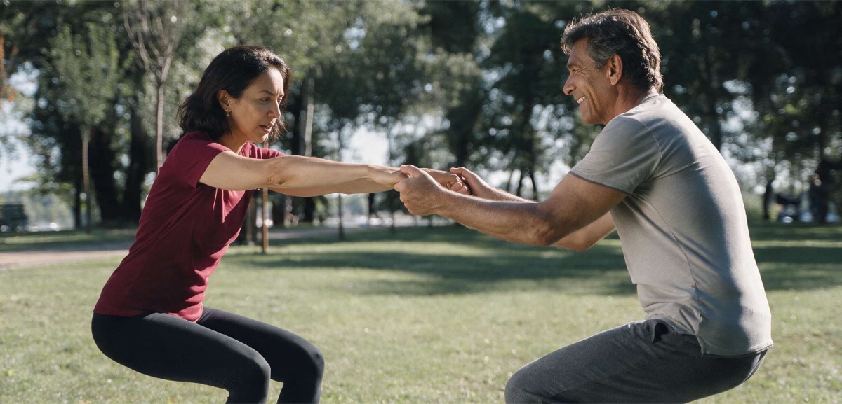 Pareja de adultos mayores haciendo sentadillas asistidas tomados de las manos