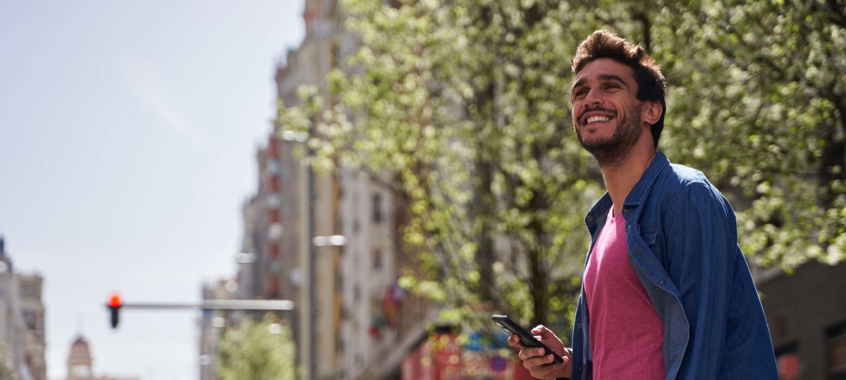 Hombre sonriendo mientras camina por la ciudad revisando su teléfono