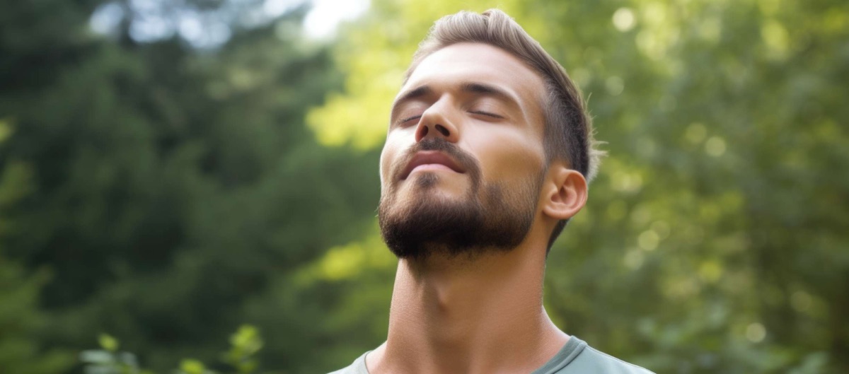 Hombre respirando con los ojos cerrados al aire libre, rodeado de árboles